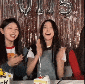 a group of young women are sitting at a table with a cake and balloons behind them .
