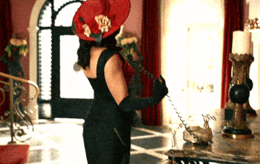 a woman in a black dress and a red hat is holding a telephone