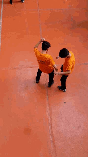 two boys in orange shirts are dancing on an orange concrete floor