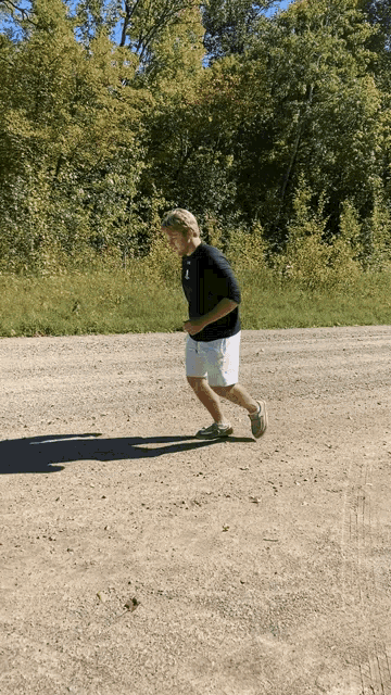 a man in shorts and a black shirt is running on a dirt road