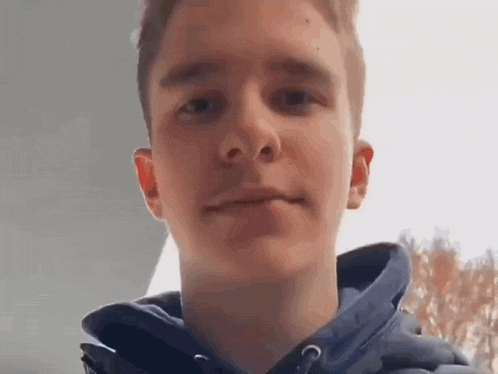 a young man wearing a blue hoodie is looking at the camera and making a funny face .