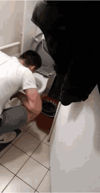 a man in a white shirt is vomiting into a toilet bowl