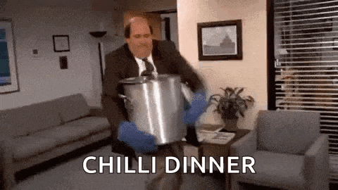 a man in a suit and tie is carrying a pot of chili dinner in a living room .