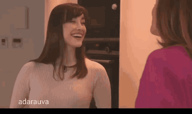 a woman in a white sweater is smiling next to another woman in a pink shirt