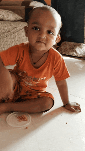 a young boy wearing an orange shirt that says star is sitting on the floor