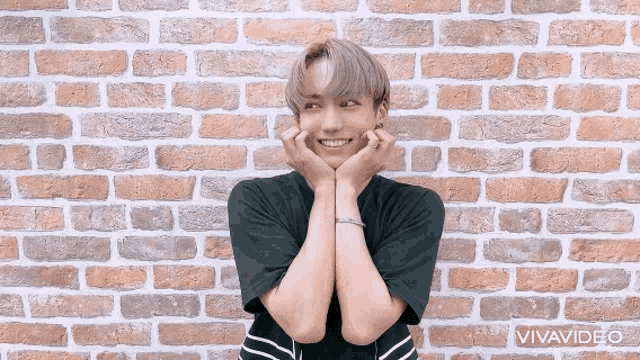 a man with his hands on his face is standing in front of a brick wall