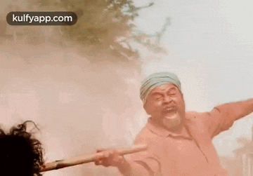 a man with a beard is holding a stick in front of a smokey background .