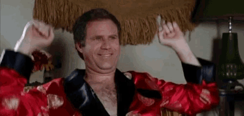 a shirtless man in a red robe is raising his arms in the air .
