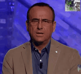 a man wearing glasses and a tan jacket is standing in front of a blue background