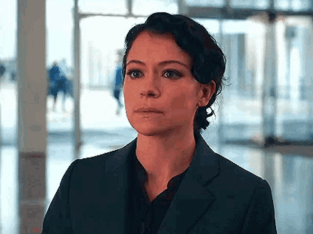 a woman in a suit and a black shirt is standing in a hallway .