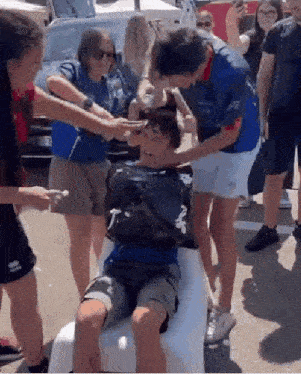 a group of people are standing around a boy who is sitting on a white chair .