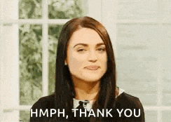 a woman is making a face and saying `` hmph , thank you '' while sitting in front of a window .
