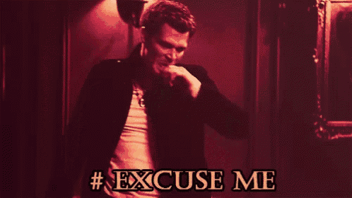 a man in a leather jacket is standing in a dark room with the words # excuse me above him
