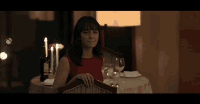a woman in a red dress is sitting at a table with candles and wine glasses