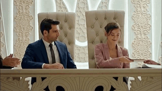 a man and a woman are sitting at a table signing papers .