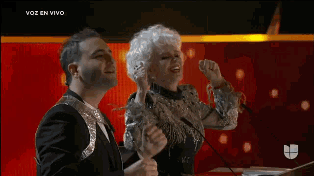 a man and a woman singing into microphones with the words voz en vivo on the bottom