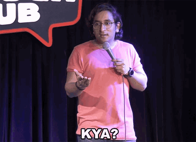 a man in a pink shirt stands in front of a microphone and says " kya "