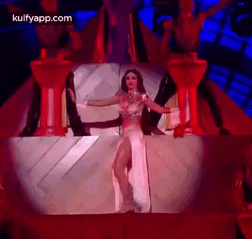 a woman in a white dress is dancing on a stage in front of a pyramid .