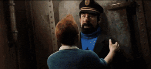 a man with a beard wearing a hat and a blue sweater is talking to another man