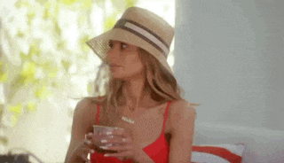 a woman in a red bikini and a straw hat is sitting on a couch holding a cup of coffee .