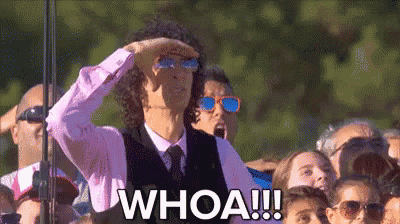 a man wearing sunglasses and a pink shirt is standing in front of a crowd and says whoa .