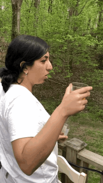 a woman in a white shirt is drinking from a glass on a deck