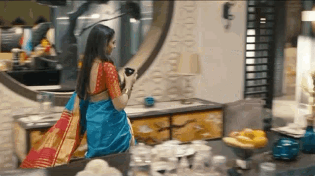 a woman in a blue and red saree is standing in front of a mirror in a room .