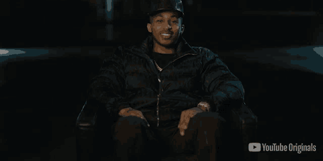 a man in a black jacket is sitting in a chair with a youtube originals logo behind him