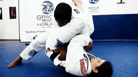 two people are wrestling in front of a sign that says grace jiu-jitsu morun
