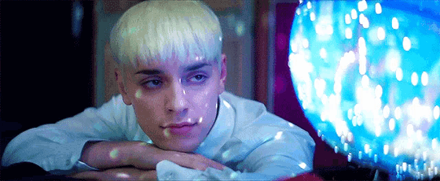 a young man with blonde hair is laying on the floor with his head on his hands .
