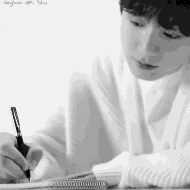 a black and white photo of a man writing in a notebook with a pen .