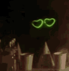 a person wearing glow in the dark heart shaped glasses is sitting at a table with cups .