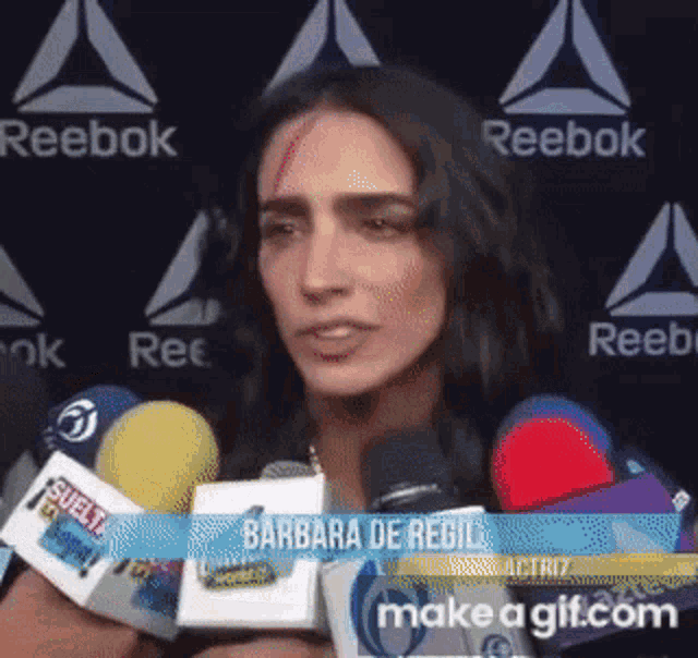 a woman with a bandage on her face is talking into microphones in front of reebok logos .