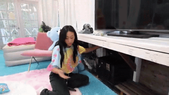 a young girl is kneeling on the floor in front of a flat screen tv .