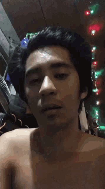 a shirtless man is making a funny face in a room with christmas lights on the ceiling .