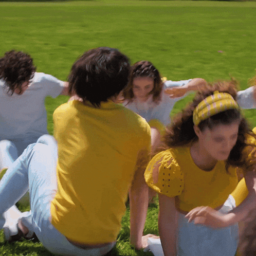 a group of people in yellow shirts are sitting in a circle on the grass