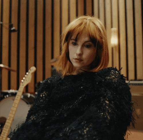 a woman in a black sweater sits in front of a drum set