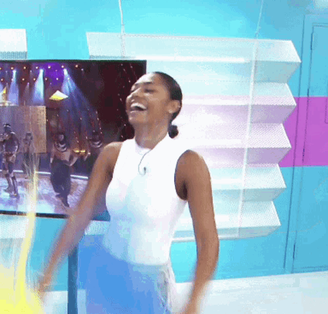 a woman in a white tank top is laughing in front of a tv
