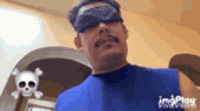 a man wearing a bandana and a blue shirt is standing in front of a skull .