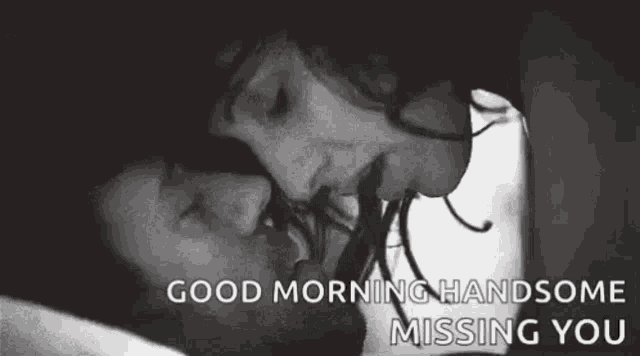 a black and white photo of a man and woman kissing in bed .
