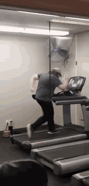 a man is running on a treadmill in a gym with a fan on the wall behind him