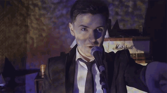 a man in a suit and tie is singing into a microphone while holding a glass
