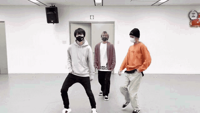 three men wearing face masks are dancing together in a room