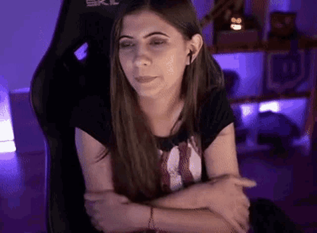 a woman is sitting in a gaming chair with her arms crossed and wearing headphones .