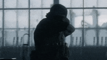 a silhouette of a person sitting in front of a window with their head in their hands .