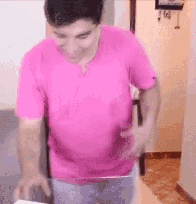a man in a pink shirt is standing in a room holding a piece of paper .