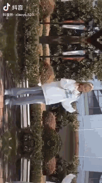 a woman in a white jacket is standing in front of a building and trees