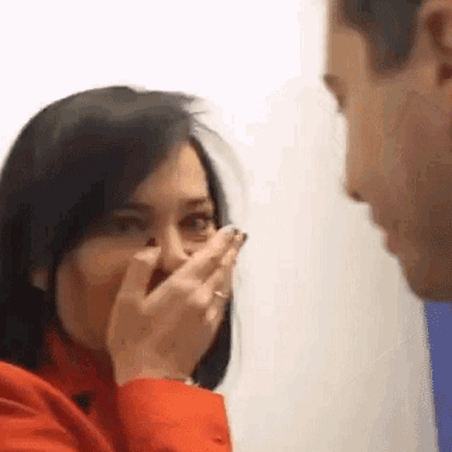 a woman in a red jacket is covering her mouth with her hands while a man looks on .