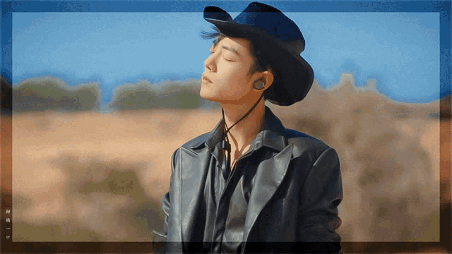 a man wearing a cowboy hat and ear buds is standing in the desert
