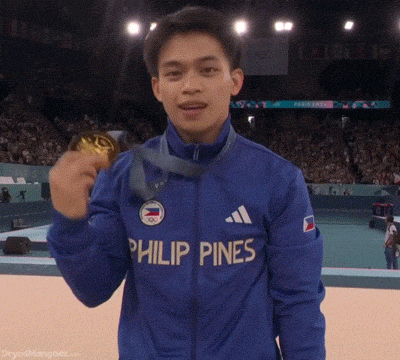 a man wearing a blue jacket that says philip pines is holding a gold medal